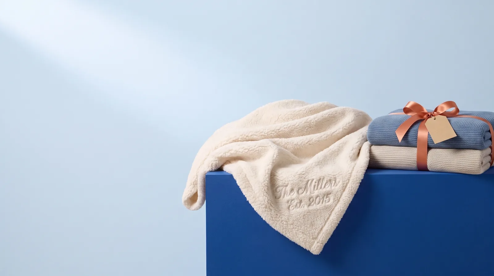 Cream sherpa blanket embroidered with a family name beside a ribbon-tied stack of blankets